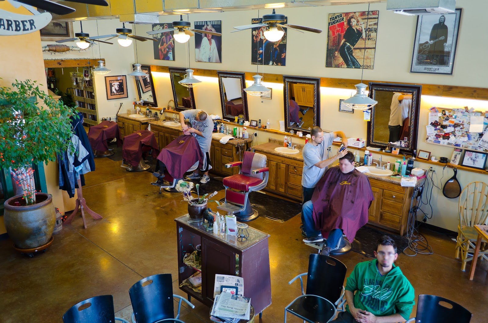 The Swade Barbershop floor: barbers cutting at vintage chairs under Edison pendants, with Johnny Cash and Tanya Tucker posters on the walls.