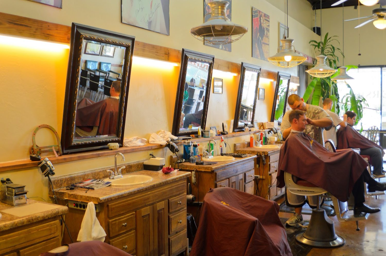 A row of carved wood mirrors and barber stations along the wall, a barber trimming a client in a maroon Swade cape.