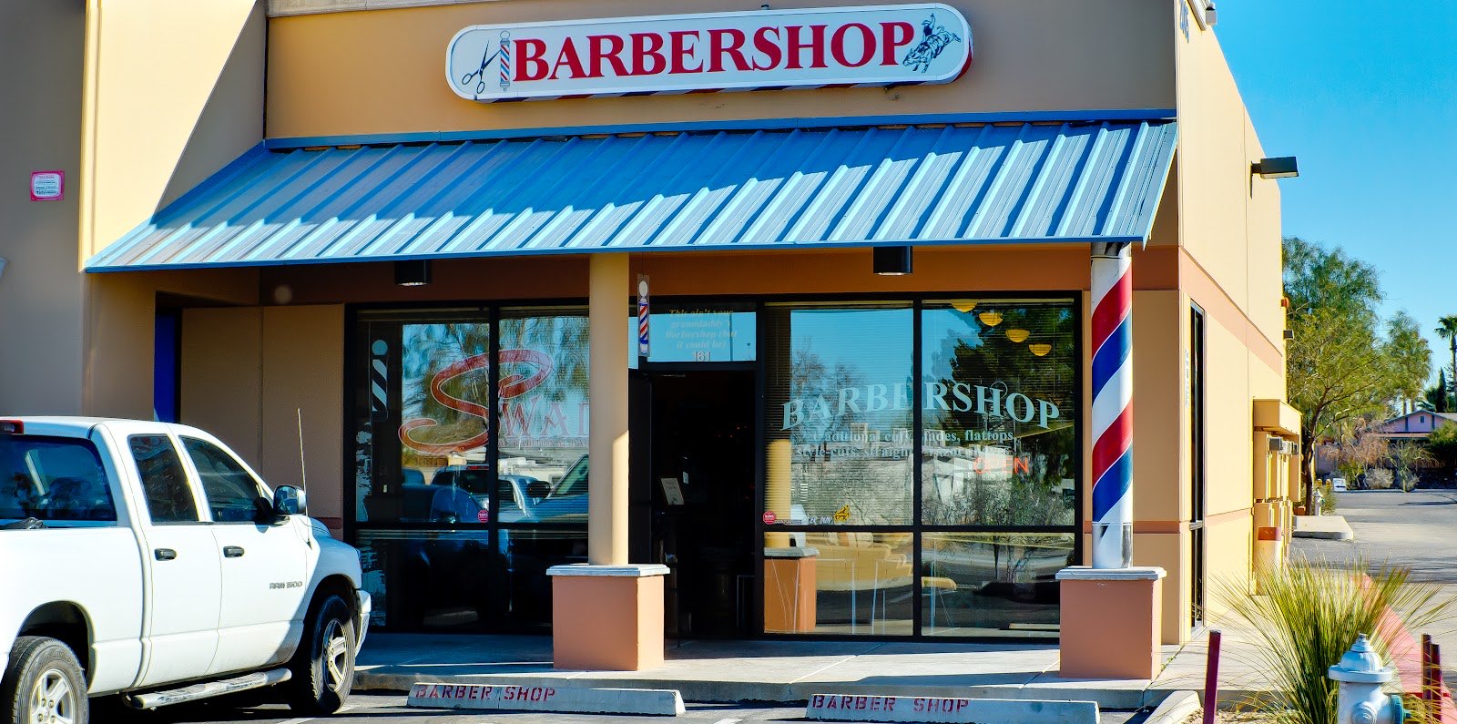 The Swade Barbershop storefront on Ruthrauff Road with its red, white and blue barber pole and painted BARBERSHOP sign.