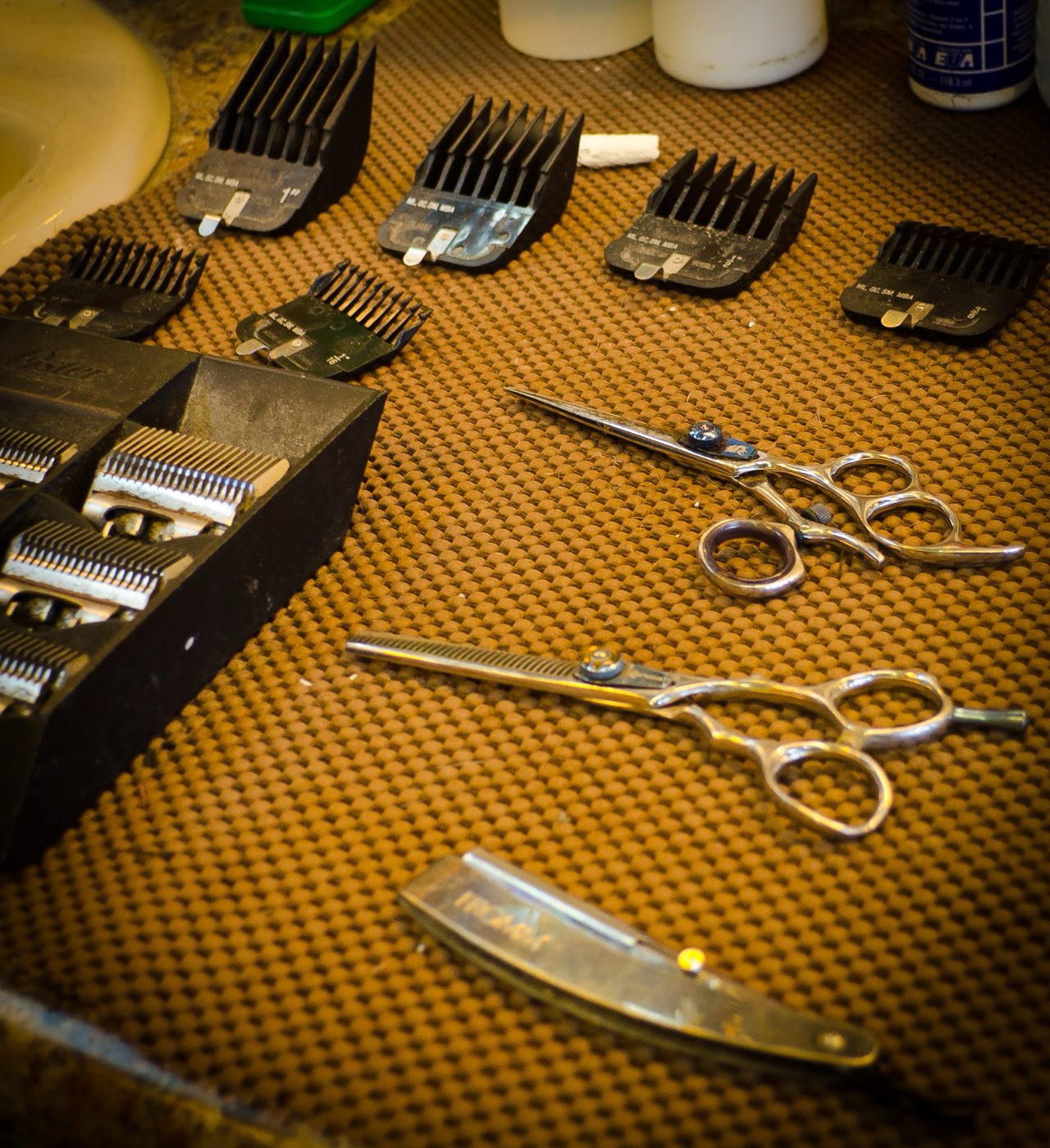 Clipper guards, shears and a straight razor laid out on a barber's mat.